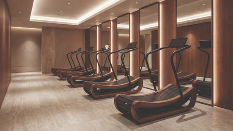 A row of wooden NOHRD Sprintbok self-powered running machines in a luxury fitness centre with warm wood paneling, mirrors, and light-coloured flooring.