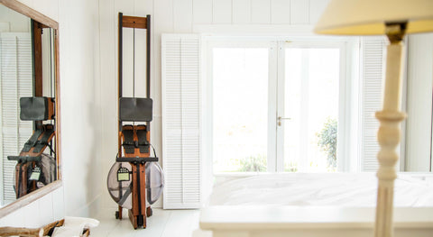 Rowing machine standing up right in the corner of a bright bedroom.